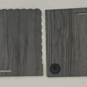 May include: Two dark gray wood-grain panels. The left panel has a scalloped top edge and a horizontal slot at the bottom. The right panel features a horizontal slot at the top, two black circular feet at the bottom, and a circular pink logo with mk.