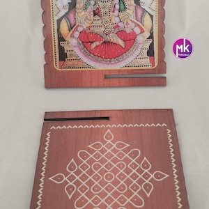 May include: Two square wooden plaques with scalloped edges. One plaque features a colorful illustration of a deity seated on a lotus, flanked by two elephants. The other plaque displays a white geometric kolam pattern on a brown wood surface.