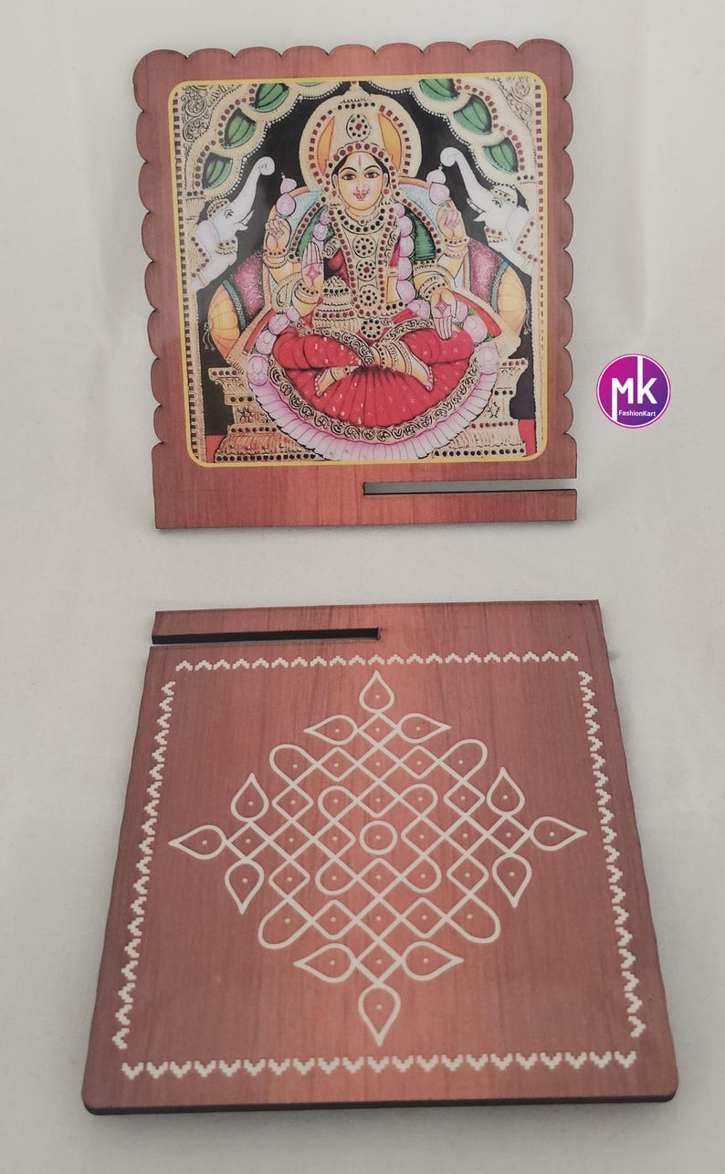 May include: Two square wooden plaques with scalloped edges. One plaque features a colorful illustration of a deity seated on a lotus, flanked by two elephants. The other plaque displays a white geometric kolam pattern on a brown wood surface.