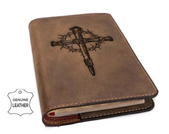 Puede incluir: Una funda de diario de cuero marrón con un diseño grabado oscuro de una cruz envuelta en una corona de espinas. La funda tiene costuras visibles en los bordes y una etiqueta blanca en la esquina con el texto GENUINE LEATHER.