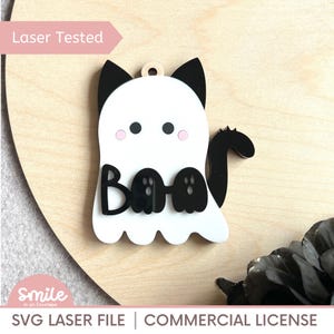 May include: A white and black Halloween-themed decoration in the shape of a ghost with cat ears and a tail. The word "Boo" is written across the ghost's body. The text "Laser Tested" and "SVG Laser File | Commercial License" are also visible.
