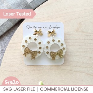 May include: White wreath earrings with gold glitter and bows. The earrings are displayed on a white card with the text "Smile in an Envelope". The words "Laser Tested" and "SVG LASER FILE | COMMERCIAL LICENSE" are also visible.