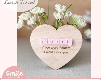 May include: A wooden heart-shaped vase with the words "mommy if you were flowers i would pick you" engraved on it. The vase is decorated with pink letters spelling out "mommy".