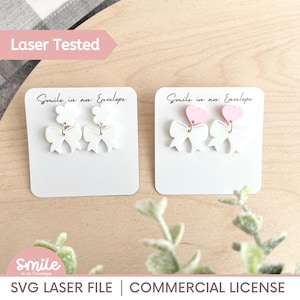 Puede incluir: Dos pares de pendientes en tarjetas blancas. Uno presenta lazos blancos y flores, el otro lazos blancos y corazones rosas. El texto "Smile in an Envelope" está arriba. En la parte inferior, "SVG LASER FILE | COMMERCIAL LICENSE."