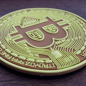 May include: A round, two-tone Bitcoin coin with a brown center and a light green outer layer. The coin features the Bitcoin symbol and text around the edge, including "FINE COPPER" and "PEER TO PEER".