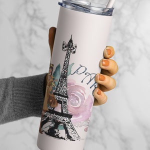 Puede incluir: Un vaso de acero inoxidable blanco con un dise&ntilde;o rosa y negro que presenta la Torre Eiffel, una mujer con un vestido y la palabra "Par&iacute;s". El vaso tiene una tapa transparente y una pajita.