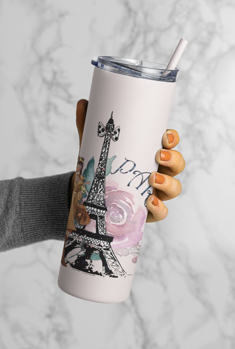 Puede incluir: Un vaso de acero inoxidable blanco con un dise&ntilde;o rosa y negro que presenta la Torre Eiffel, una mujer con un vestido y la palabra "Par&iacute;s". El vaso tiene una tapa transparente y una pajita.