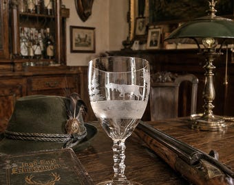 Könnte beinhalten: Ein Weinglas aus klarem Glas mit einer geätzten Darstellung eines Jagdhundes in einer Waldlandschaft. Der Stiel des Glases weist eine facettierte, mehrstufige Struktur auf, und der Kelch ist glatt mit einer detaillierten Gravur eines Hundes.