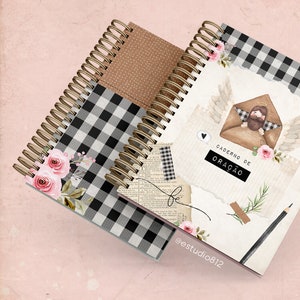 May include: Two spiral bound notebooks with black and white checkered covers. One notebook has a brown cover with white polka dots. The front cover of the other notebook features a watercolor illustration of an angel holding a brown envelope with a person inside. The text on the cover reads "Caderno de Ora&ccedil;&atilde;o" and "@estudio812".