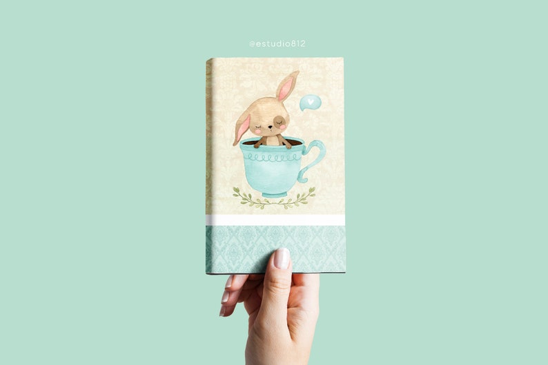 May include: A rectangular canvas print featuring a whimsical illustration of a bunny nestled inside a light blue teacup. The bunny has closed eyes and long ears. The teacup is decorated with a floral design. The background is a light beige with a floral pattern.