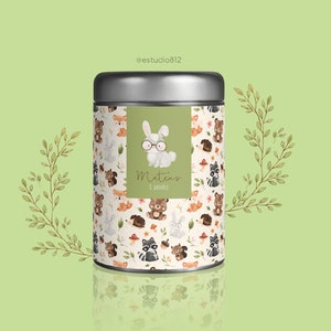 May include: A silver metal container with a green label featuring a cartoon bunny wearing glasses. The label says "Mateus 1 ano". The container is decorated with a pattern of woodland animals, including foxes, bears, raccoons, and squirrels.