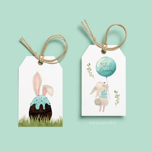 May include: Two white gift tags with watercolor illustrations. One features a bunny with an Easter egg, the other a bunny holding a balloon with the text "Feliz P&aacute;scoa". Both tags have twine for hanging.