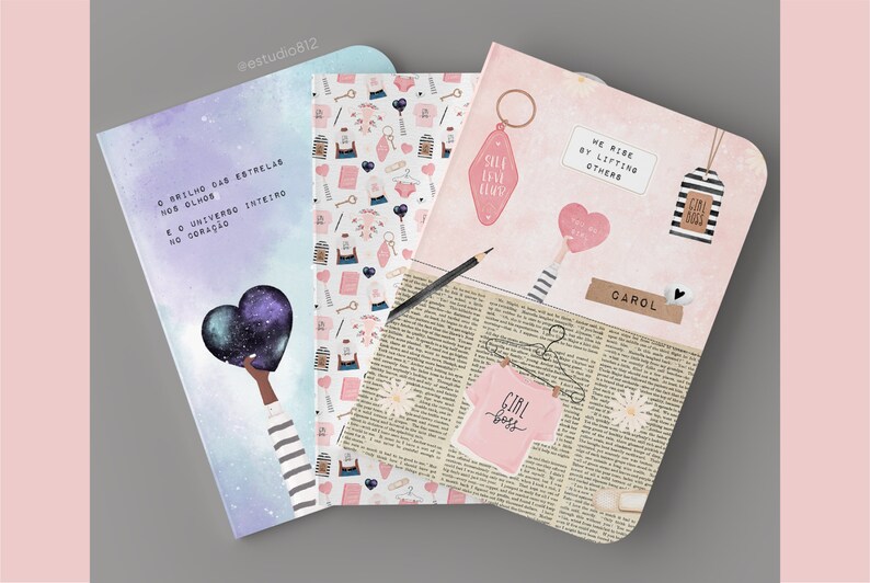 May include: Three pink and white notebooks with different designs. The first notebook has a galaxy design with the text "O brilho das estrelas nos olhos e o universo inteiro no cora&ccedil;&atilde;o". The second notebook has a pink and white pattern with hearts, keys, and other small objects. The third notebook has a pink background with a newspaper print and the text "We rise by lifting others" and "Girl Boss".