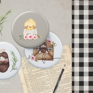 May include: Three round buttons with religious imagery. The first button has a gray background with a yellow chick and pink flowers. The second button has a white background with a brown-haired man with a halo and a green leafy border. The third button has a white background with a brown-haired man in a brown envelope with the word "fe" written on it.