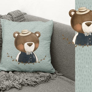 Puede incluir: Una almohada azul claro con un oso marr&oacute;n que lleva un sombrero y un chaleco. El oso est&aacute; rodeado de hojas verdes. La almohada tiene un patr&oacute;n moteado sutil.