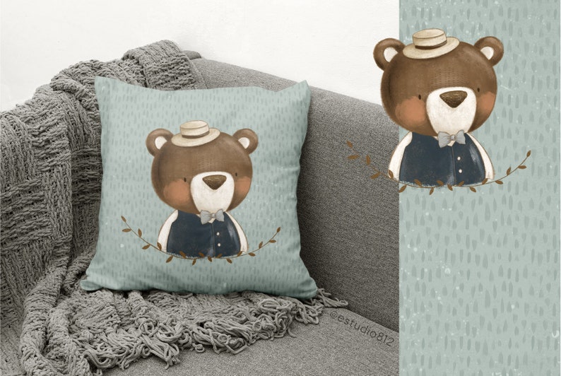 Puede incluir: Una almohada azul claro con un oso marr&oacute;n que lleva un sombrero y un chaleco. El oso est&aacute; rodeado de hojas verdes. La almohada tiene un patr&oacute;n moteado sutil.