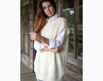 May include: A white knitted sleeveless sweater with a turtleneck collar. The sweater is loose fitting and has a ribbed texture.