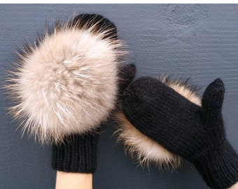 Puede incluir: Un par de guantes de punto negros con pompones de piel marrón y blanca.