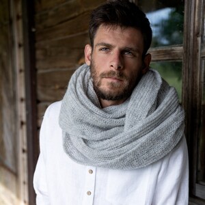 May include: A man wearing a white linen shirt with wooden buttons and a gray knitted scarf. He is sitting on a wooden porch.