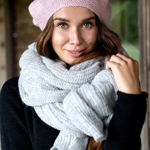 May include: A woman wearing a pink knitted beret and a gray knitted scarf. The scarf is wrapped around her neck and shoulders.