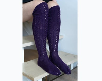 May include: Purple knitted knee-high socks with a lacy pattern. The socks are worn on a person's legs.