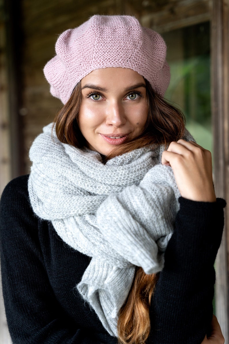 May include: A woman wearing a pink knitted beret and a gray knitted scarf. The scarf is wrapped around her neck and shoulders.