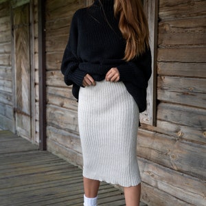 K&ouml;nnte beinhalten: Eine Frau tr&auml;gt einen schwarzen Rollkragenpullover und einen beigefarbenen gerippten Strickrock. Sie steht vor einer Holzwand und tr&auml;gt braune Stiefel.