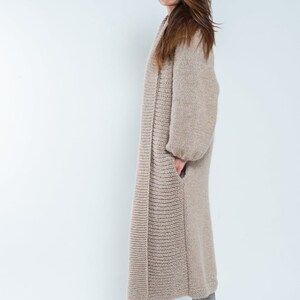 May include: A long, beige knitted cardigan with a relaxed fit and long sleeves. The cardigan is open in the front and has a slightly textured knit.