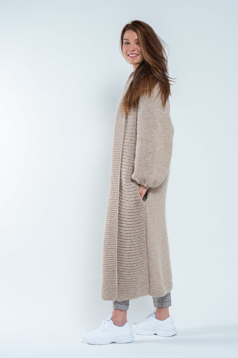 May include: A long, beige knitted cardigan with a relaxed fit and long sleeves. The cardigan is open in the front and has a slightly textured knit.