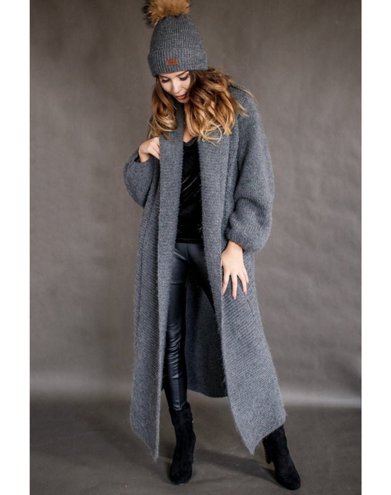 May include: A long, gray knitted cardigan with a shawl collar and long sleeves. The cardigan is made of a soft, fuzzy yarn and has a relaxed fit.