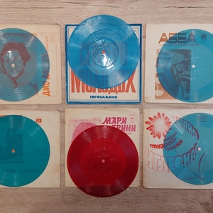 Könnte beinhalten: Sechs Vintage-Vinylplatten mit Albumcovern. Die Schallplatten sind in Blau- und Rottönen gehalten. Die Albumcover zeigen Text und Bilder, darunter die Band ABBA und den Namen "Джо Дассен".