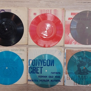 Könnte beinhalten: Sammlung von Vintage-Schallplatten. Die Schallplatten sind in verschiedenen Farben erhältlich, darunter Schwarz, Rot, Blau und Grau. Jede Schallplatte liegt auf ihrem Original-Albumcover. Die Albumcover zeigen Text und Illustrationen.