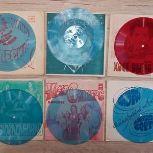 Könnte beinhalten: Eine Sammlung von sechs Vintage-Schallplatten. Die Schallplatten sind in verschiedenen Farben, darunter Blau und Rot, und weisen gedruckten Text und Grafiken auf. Die Albumcover sind in verschiedenen Farben, darunter Weiß, Grün und Rot.