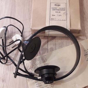 Può includere: Cuffie nere vintage con archetto circolare e padiglioni, collegate a un cavo nero con una spina bianca. Le cuffie sono accanto a una scatola di cartone e a un foglio con testo cirillico.