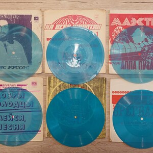 Könnte beinhalten: Eine Sammlung von Vintage-Schallplatten mit blau-transparenten Scheiben. Die Albumcover zeigen verschiedene Designs und kyrillischen Text, vor einem Holzuntergrund. Die Schallplatten sind in einer ordentlichen, organisierten Anordnung.
