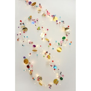 May include: A decorative string of lights with colourful sequins, beads, and small star-shaped accents. The string features warm white LED lights and is designed for festive decor. The sequins are gold, pink, purple, and green.