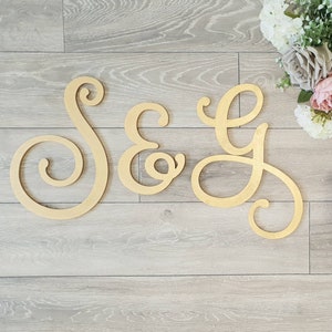 May include: S&G wooden letters in a cursive font, painted in a light gold colour. The letters are on a light wood floor.