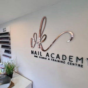 May include: A white wall with a black and rose gold sign that reads "vk Nail Academy Nail Studio & Training Centre".