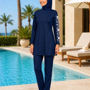 Puede incluir: Un traje de baño de cobertura completa en color azul oscuro que consta de una túnica de manga larga y pantalones a juego. La túnica presenta un patrón floral blanco a lo largo de la manga izquierda. Incluye un pañuelo a juego en azul oscuro.