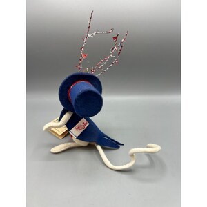 May include: A felt mouse figurine wearing a blue top hat and a matching blue tailcoat with a white lapel featuring the red text "Annalee". The mouse has a long white tail and is adorned with decorative red, white, and blue tinsel-like wire antlers.