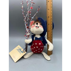 May include: A fabric mouse doll wearing a blue hat, blue vest, and red overalls with white stars. The mouse holds a decorative branch with red, white, and blue star accents. A wooden ruler shows the doll is approximately 9 inches tall.