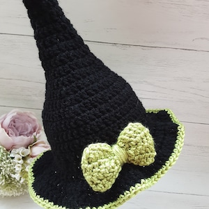 May include: A black crocheted witch hat with a green crocheted bow. The hat has a wide brim and a tall pointed crown.