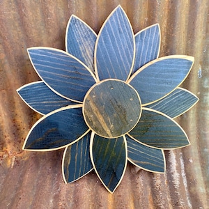May include: A wooden flower with a dark blue stain and a natural wood center. The flower has eight petals and is a rustic home decor piece.