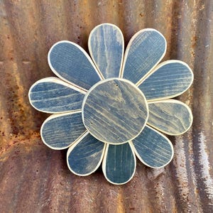 May include: A wooden daisy with eight petals painted in a dark blue color. The center of the daisy is also made of wood and is painted in a lighter shade of blue. The daisy is a rustic home decor item.