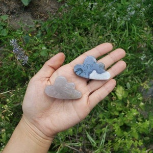 May include: Two cloud-shaped crystal paperweights, one is a light purple color and the other is a dark gray and white color.