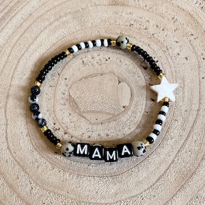 May include: Black and white beaded bracelet with a white star charm and the word "MAMA" spelled out in black letter beads.