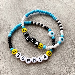 Handmade personalised beaded name bracelet. Glass beads and smiley with acrylic letters and a ceramic evil eye bead. Blue, black, yellow.
