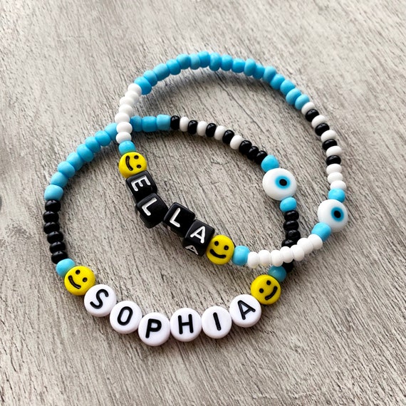Handmade personalised beaded name bracelet. Glass beads and smiley with  acrylic letters and a ceramic evil eye bead. Blue, black, yellow.