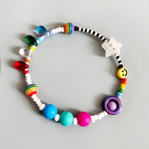 Op de afbeelding: Een kleurrijke kralen armband met regenboog, blauwe en paarse kralen, een ster bedel en een smiley bedel.