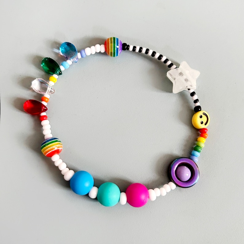 Op de afbeelding: Een kleurrijke kralen armband met regenboog, blauwe en paarse kralen, een ster bedel en een smiley bedel.